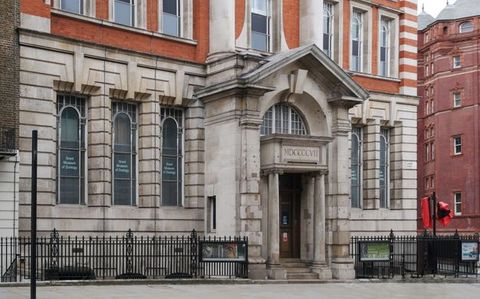 Architecture. A colour photograph shows a two-storey building is grey stone on the bottom level and red brick above. The door is under a double-high arch topped by a triangular pediment.
